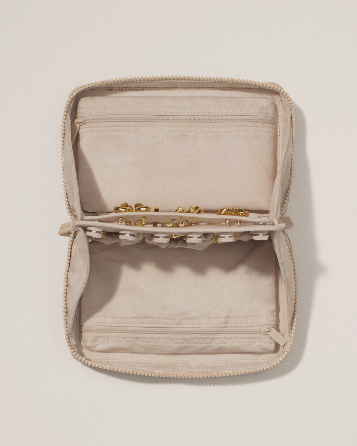 Overhead view of the Afform Bisque (white) Vault, showcasing its two-sided interior with one side for rings and earrings and the other for necklaces. Both sides have a zipper pocket for watches and bracelets. The ring and earring bars' removable feature is shown
