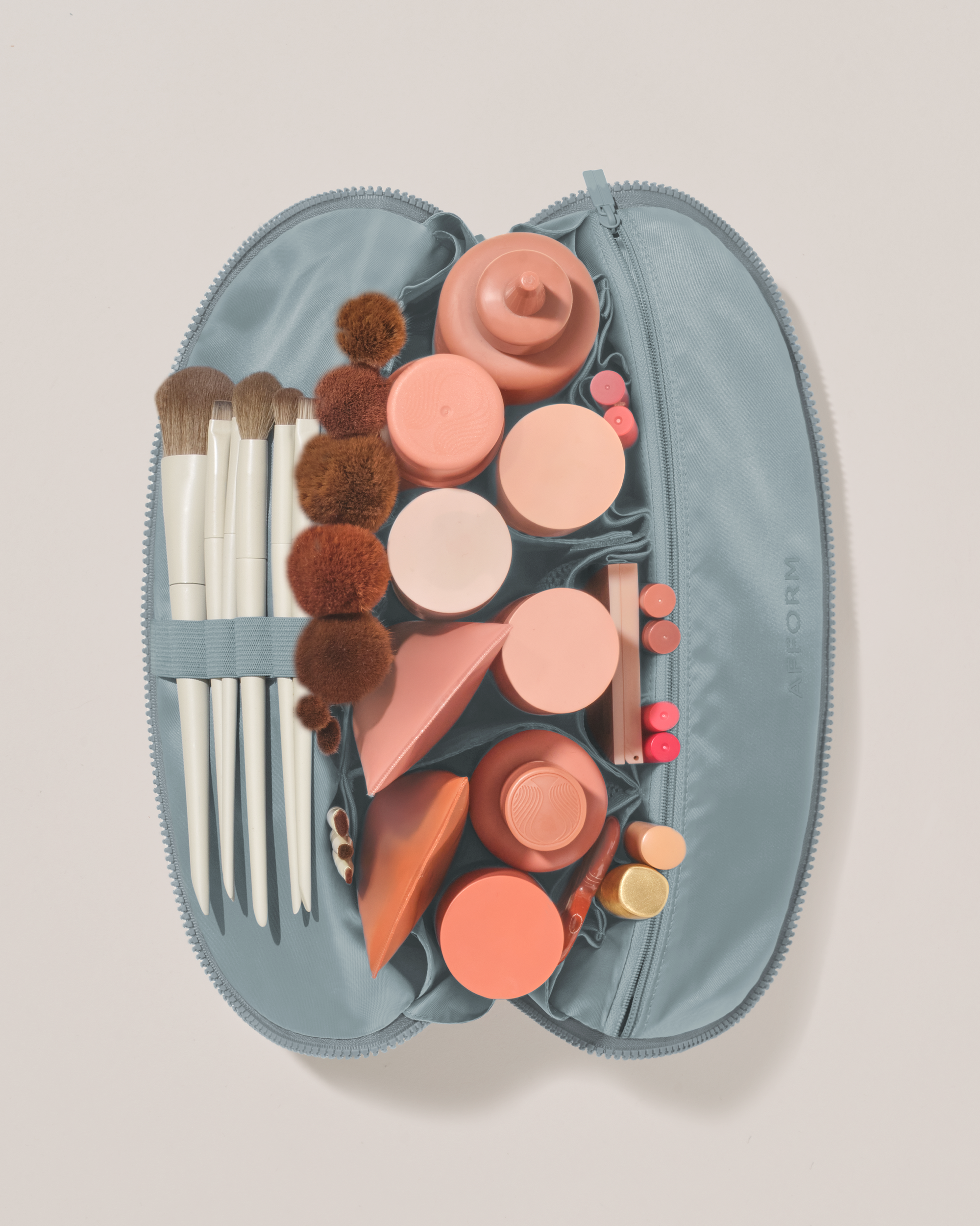 Overhead view of the Large Slate (blue) Traveller makeup bag fully packed with upright beauty products and organized compartments