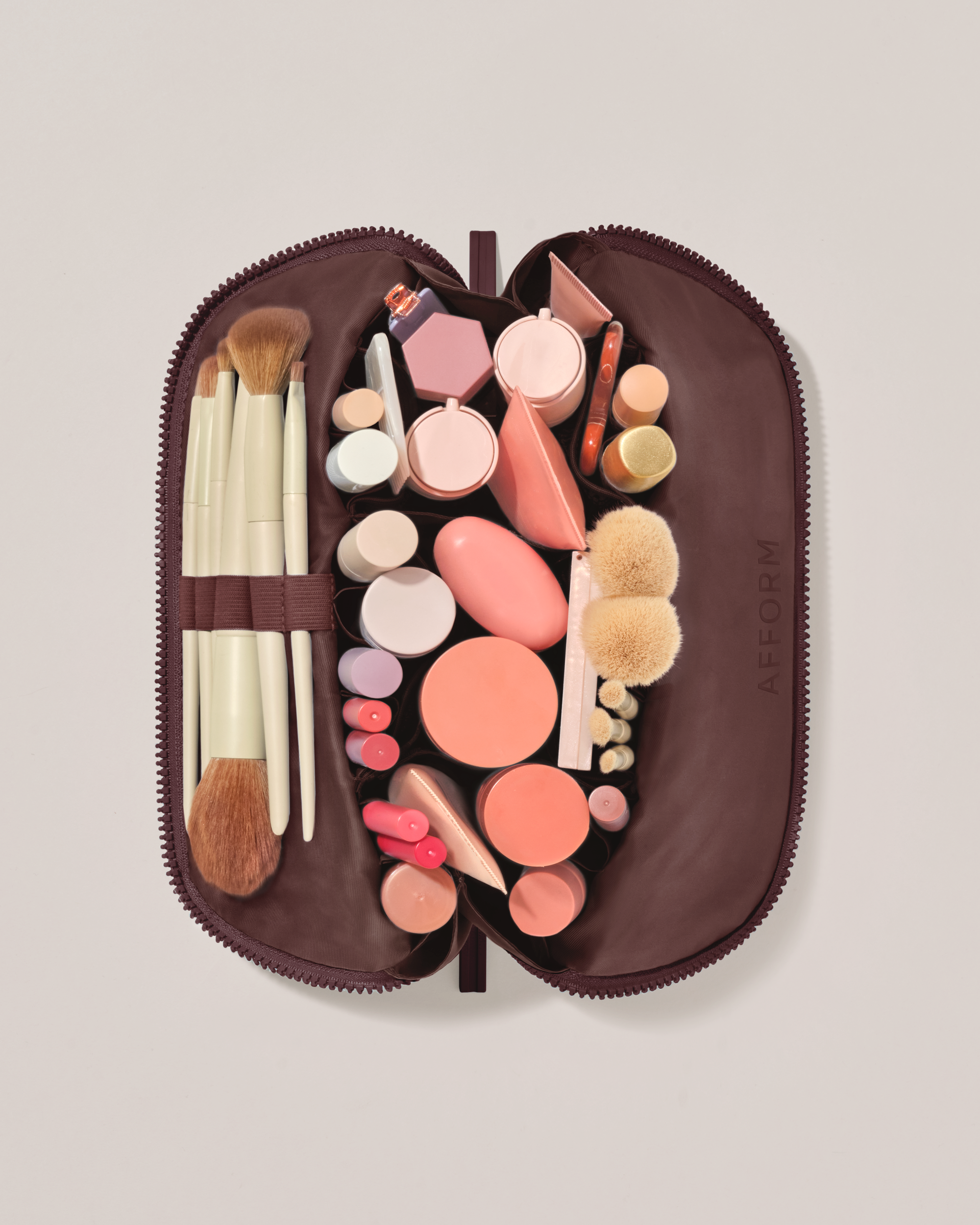 Overhead view of the Medium Cassis (maroon) Traveller makeup bag fully packed with upright beauty products and organized compartments