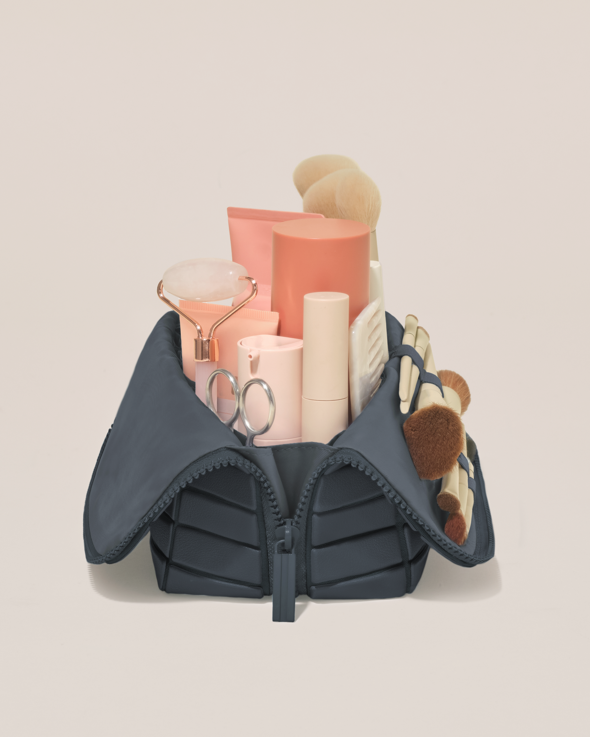 Side profile of the Medium Indigo (navy) Traveller makeup bag filled with beauty essentials standing upright, showing flexible compartment design
