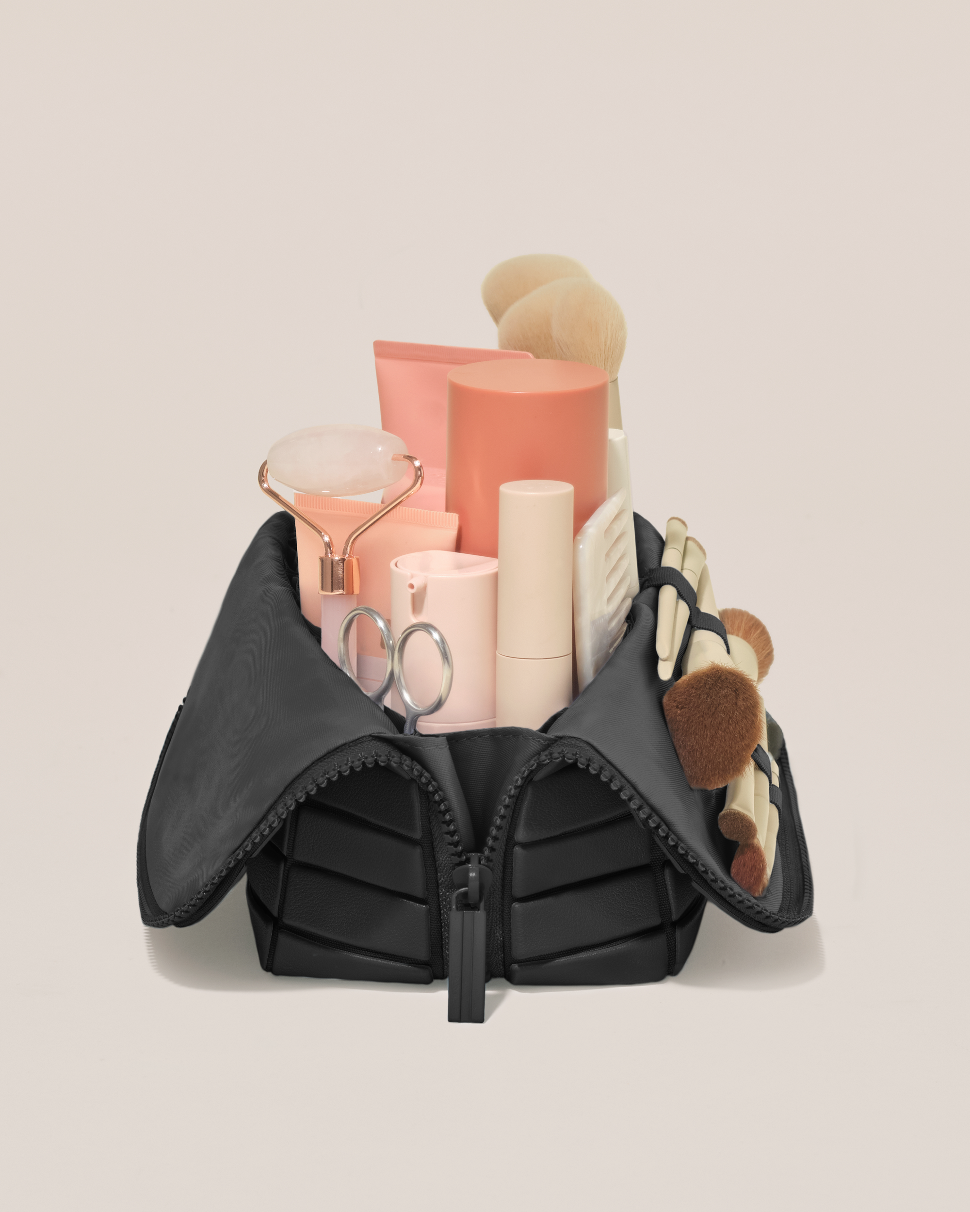 Side profile of the Medium Onyx (black) Traveller makeup bag filled with beauty essentials standing upright, showing flexible compartment design
