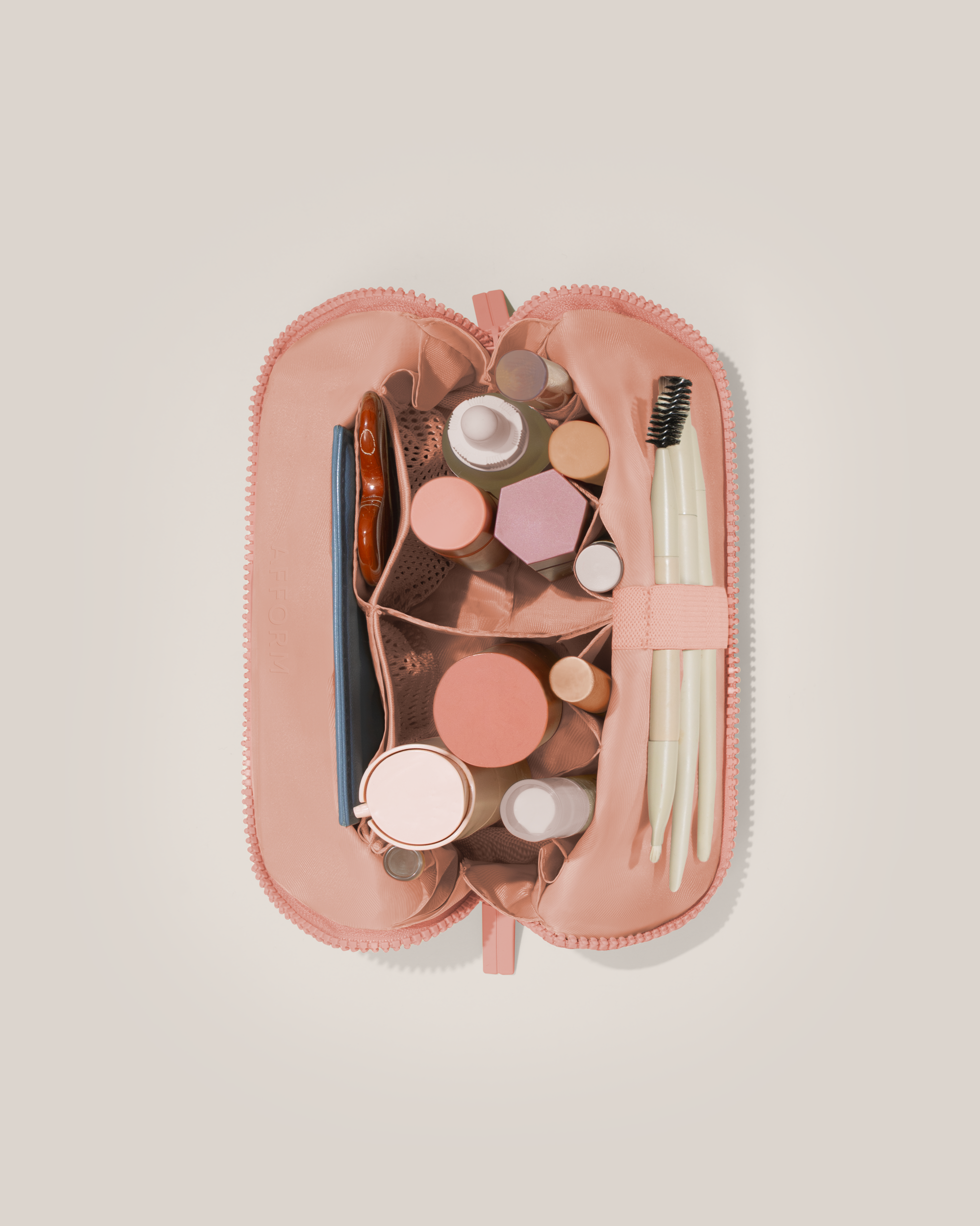 Overhead view of the Small Blush (pink) Traveller makeup bag fully packed with upright beauty products and organized compartments