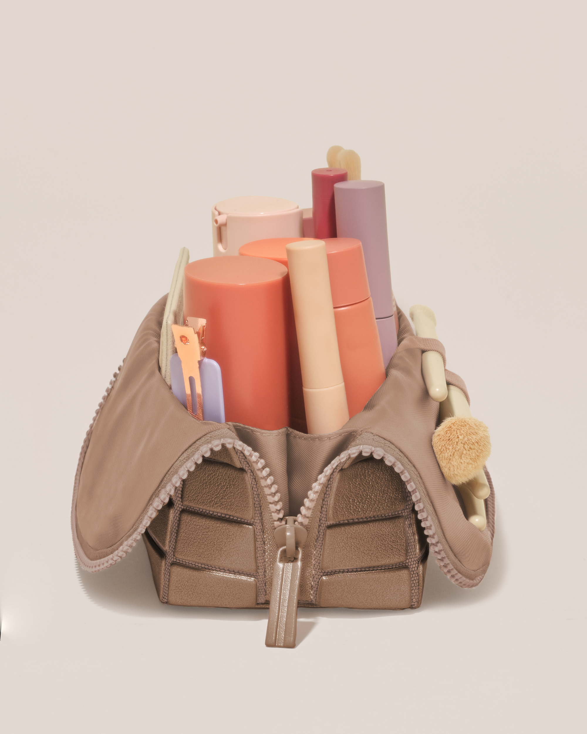 Side profile of the Small Bronze Traveller makeup bag filled with beauty essentials standing upright, showing flexible compartment design