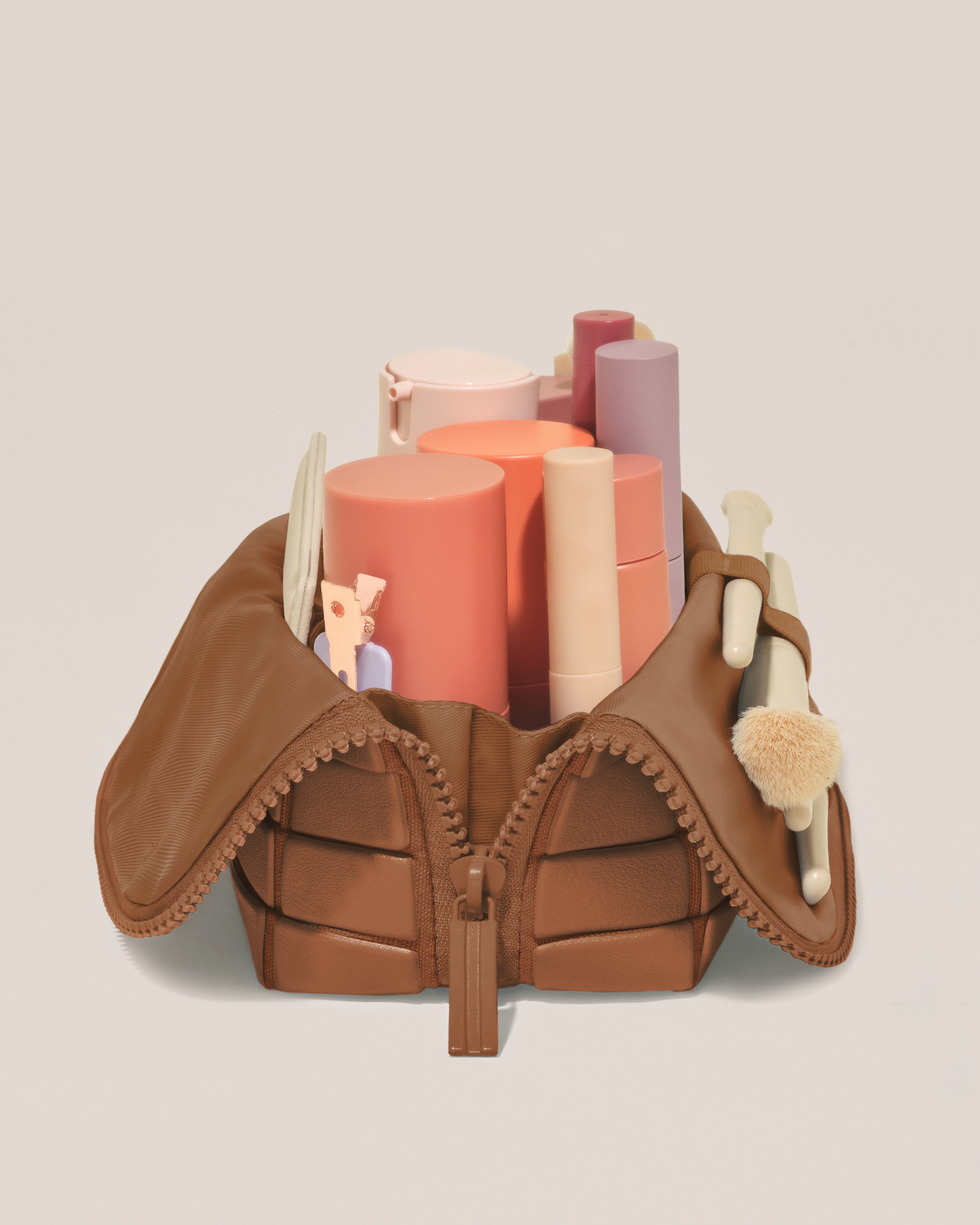 Side profile of the Small Vicuna (brown) Traveller makeup bag filled with beauty essentials standing upright, showing flexible compartment design