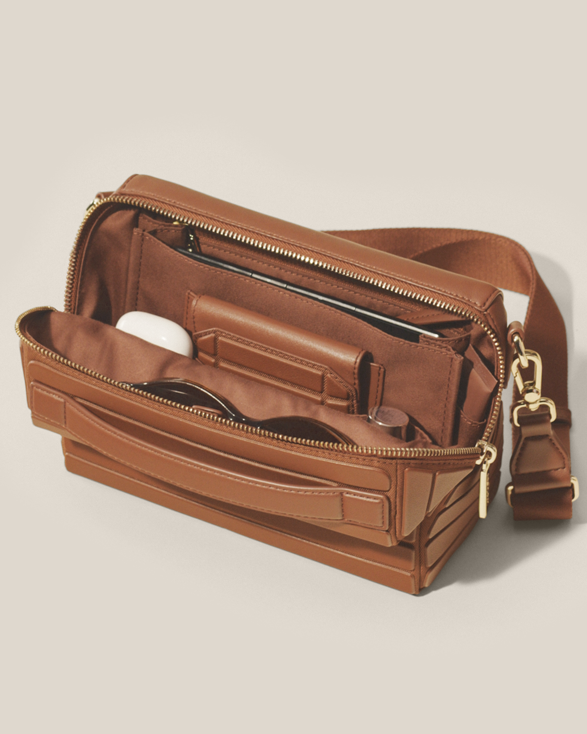 Open Afform Vicuna Crossbody bag showing earbuds, sunglasses, phone, and organized interior pockets