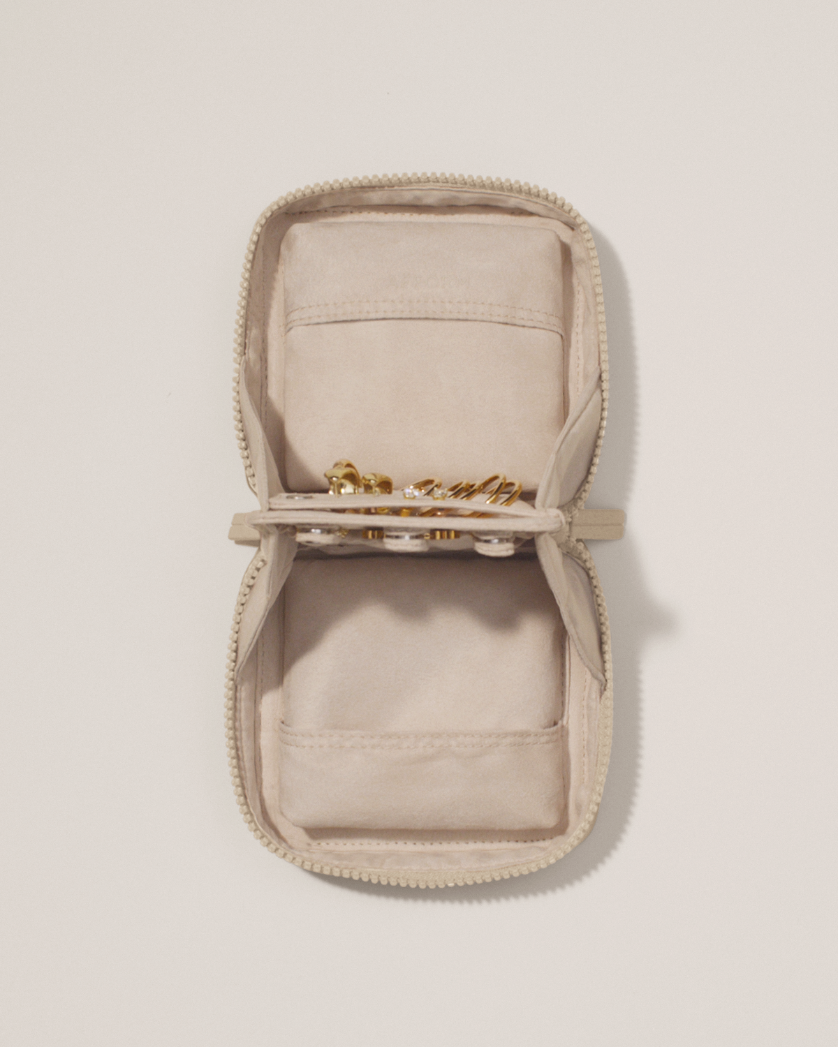 Overhead view of the Afform Small Bisque (white) Vault, showcasing its two-sided interior with one side for rings and earrings and the other for necklaces. Both sides have a zipper pocket for watches and bracelets. The ring and earring bars' removable feature is shown