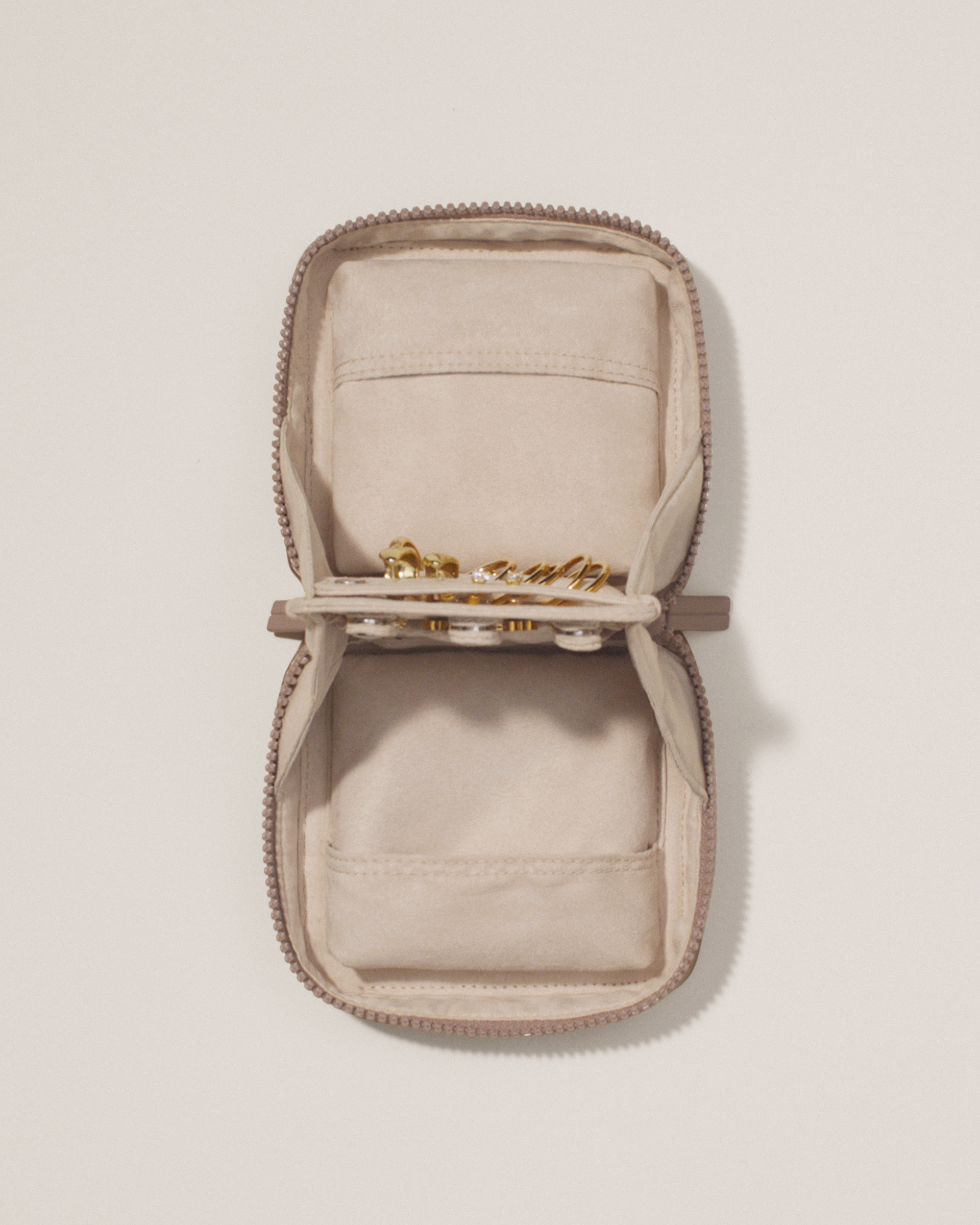 Overhead view of the Afform Small Bronze Vault, showcasing its two-sided interior with one side for rings and earrings and the other for necklaces. Both sides have a zipper pocket for watches and bracelets. The ring and earring bars' removable feature is shown
