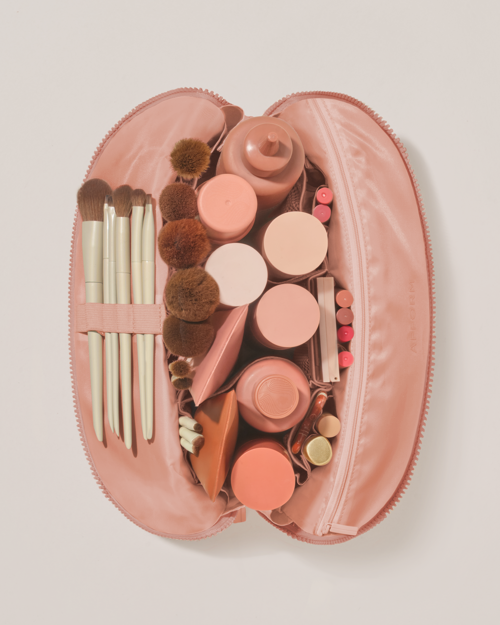 Overhead view of the Large Blush (pink) Traveller makeup bag fully packed with upright beauty products and organized compartments