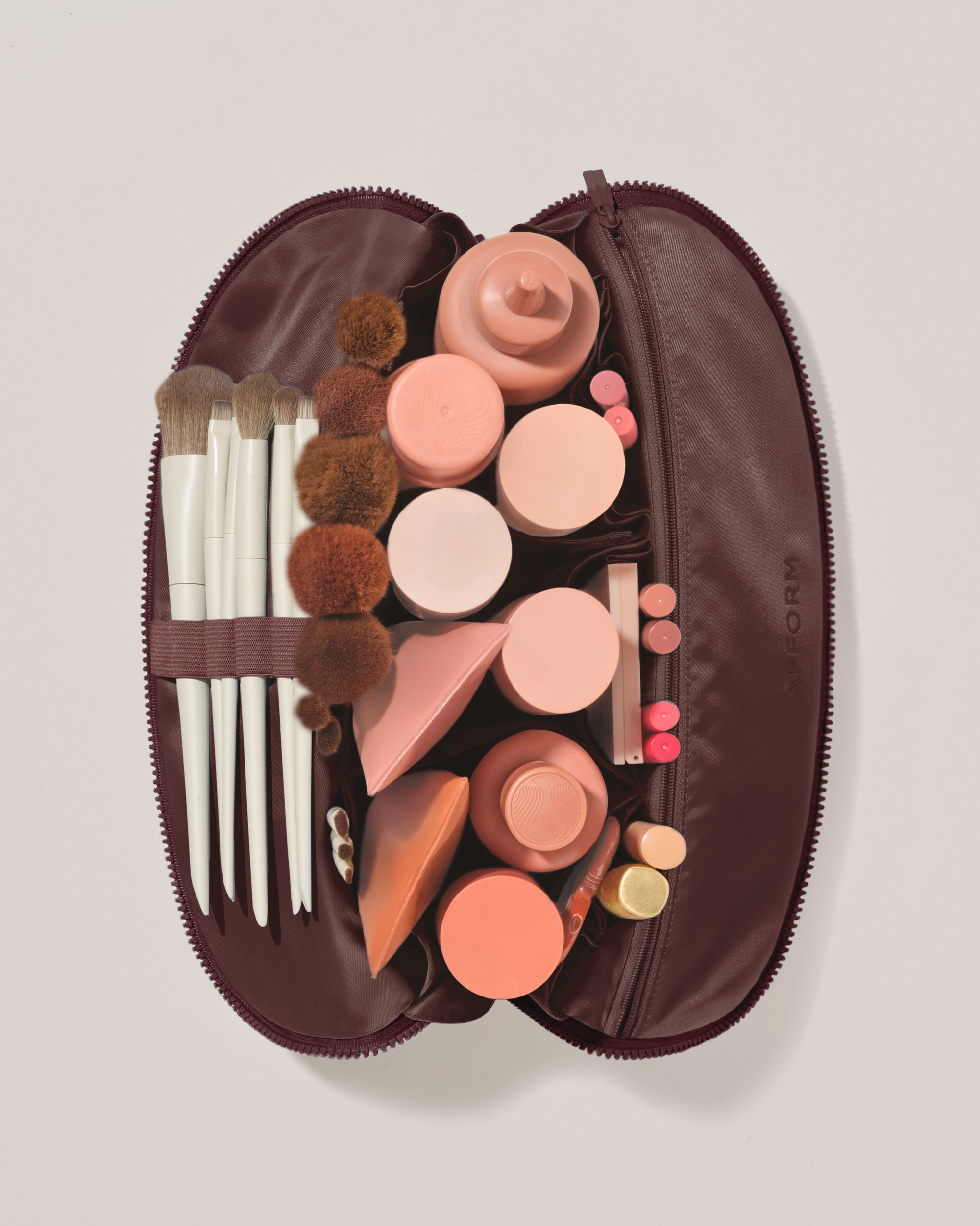 Overhead view of the Large Cassis (maroon) Traveller makeup bag fully packed with upright beauty products and organized compartments