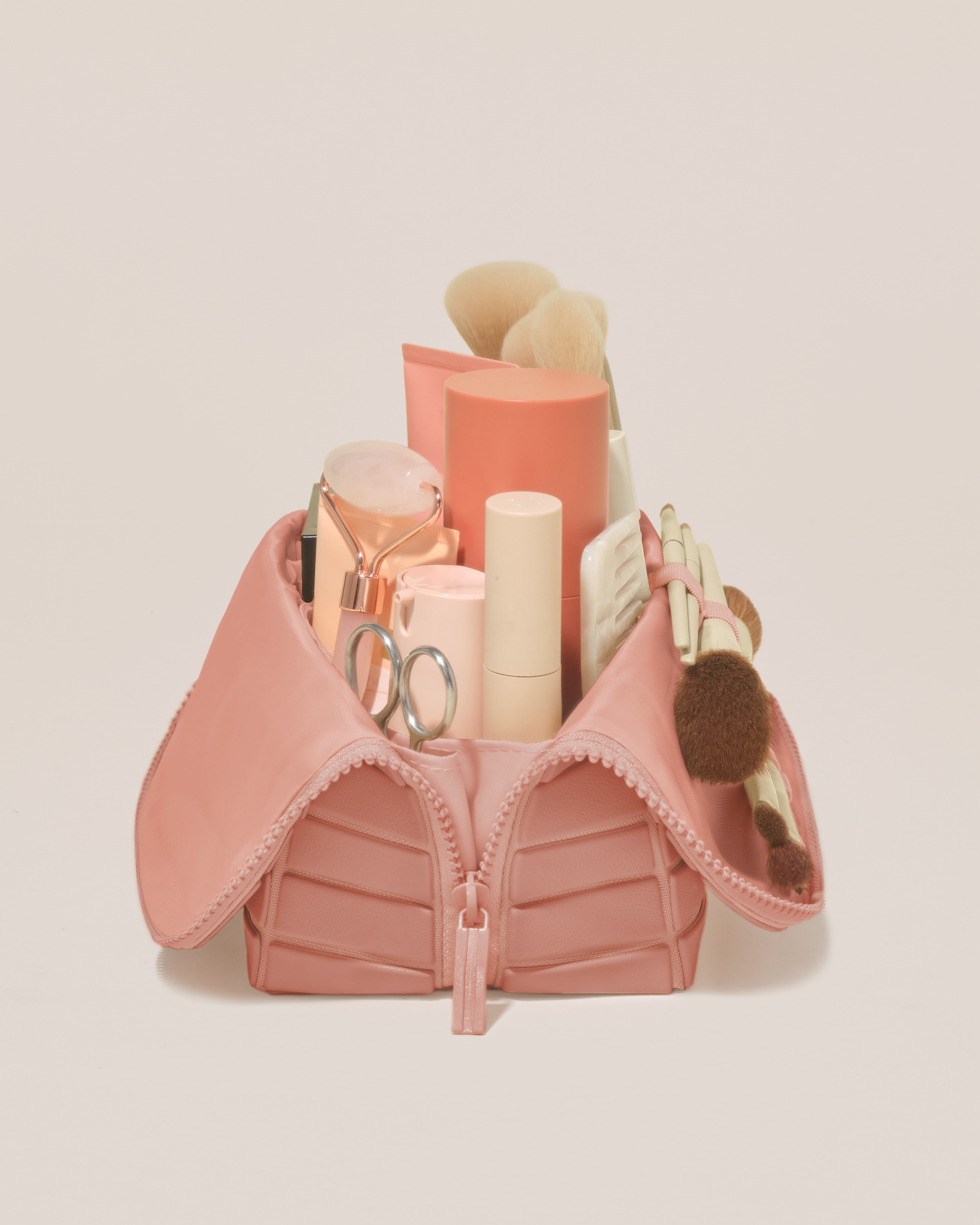 Side profile of the Medium Blush (pink) Traveller makeup bag filled with beauty essentials standing upright, showing flexible compartment design