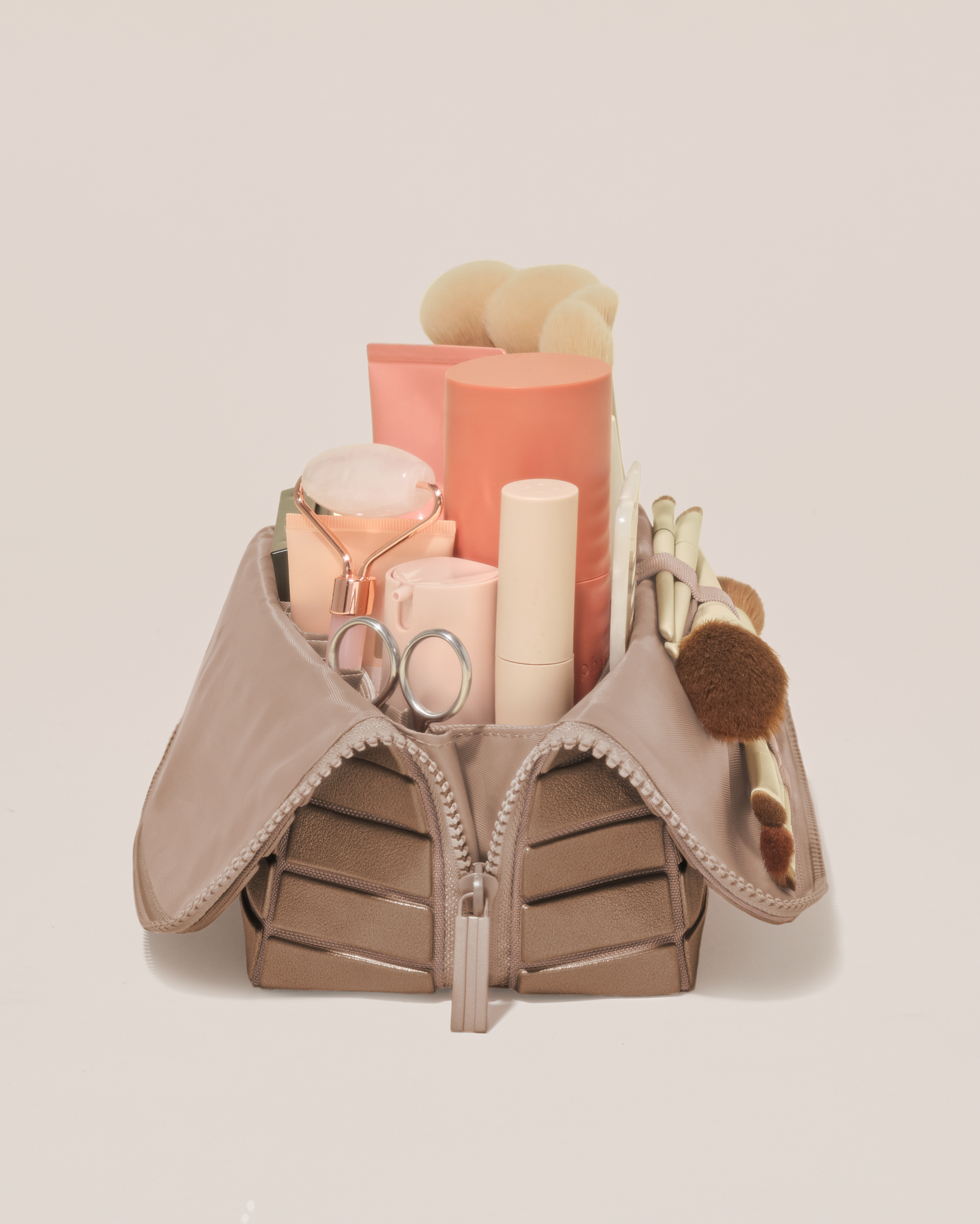Side profile of the Medium Bronze Traveller makeup bag filled with beauty essentials standing upright, showing flexible compartment design