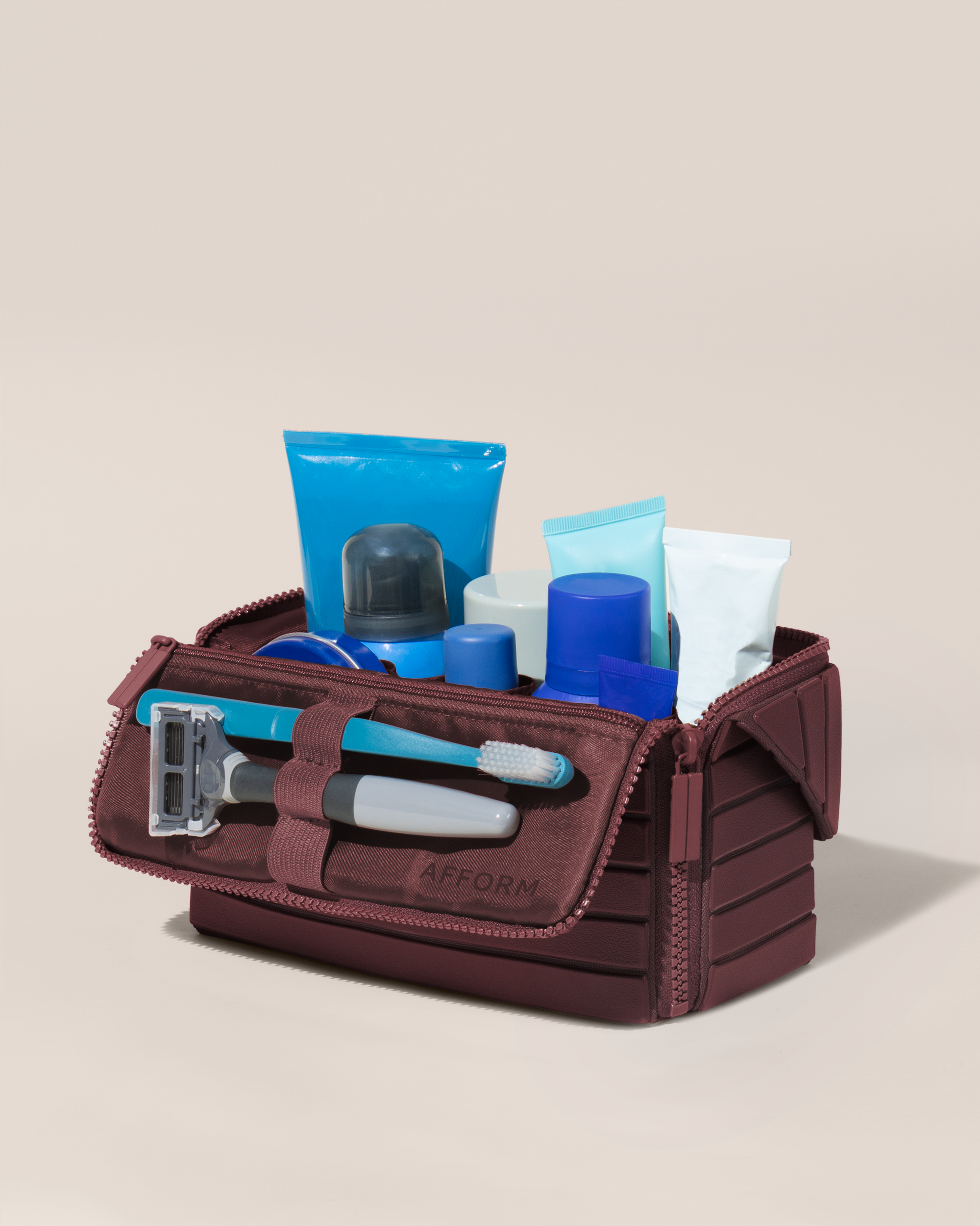 Open Afform Medium Cassis (maroon) Kit, shown open and packed with grooming essentials like razors, cologne, and skincare. A structured, travel-ready toiletry organizer