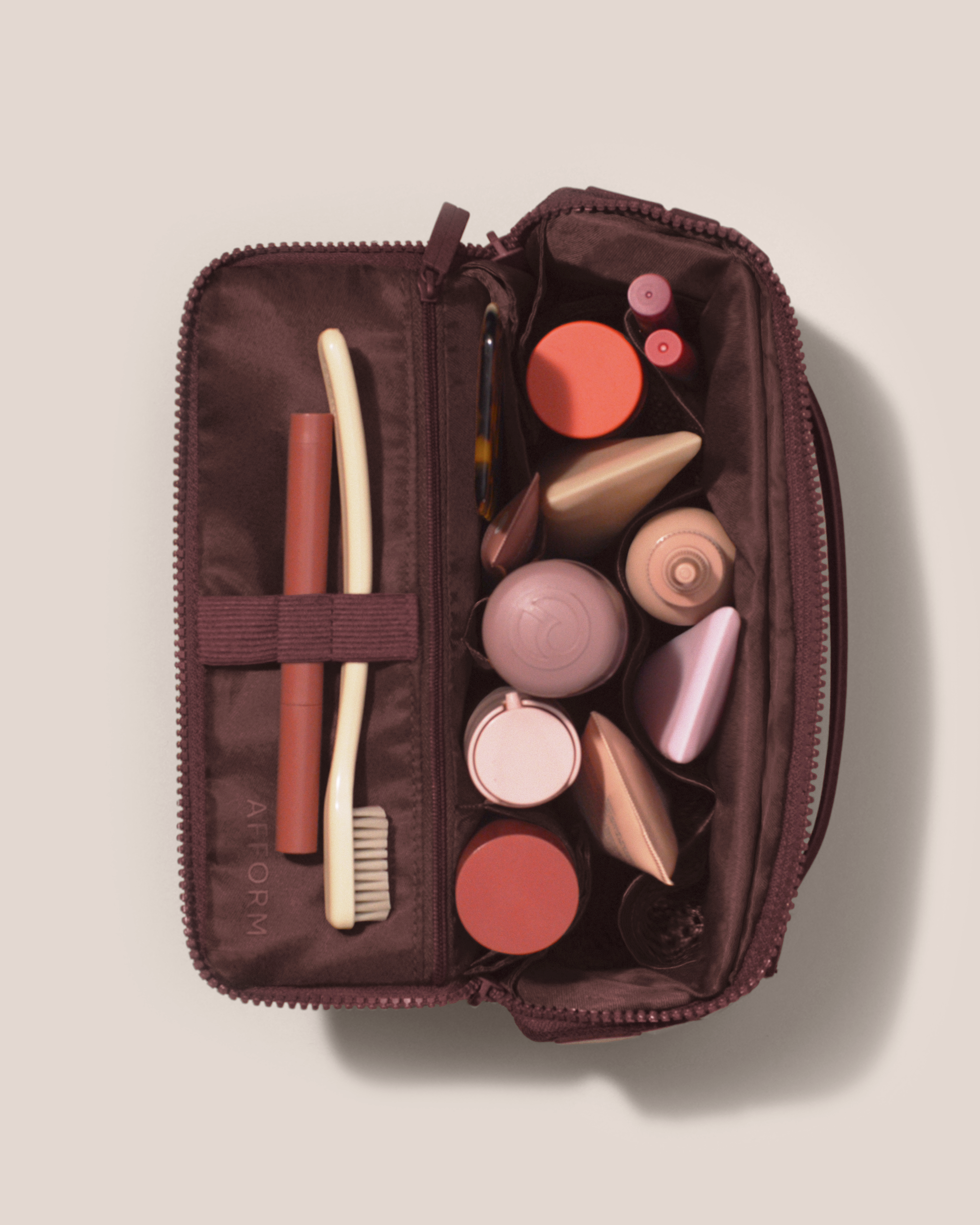 Overhead view of Afform Medium Cassis (maroon) Kit toiletry bag fully packed with upright toiletry products and organized compartments