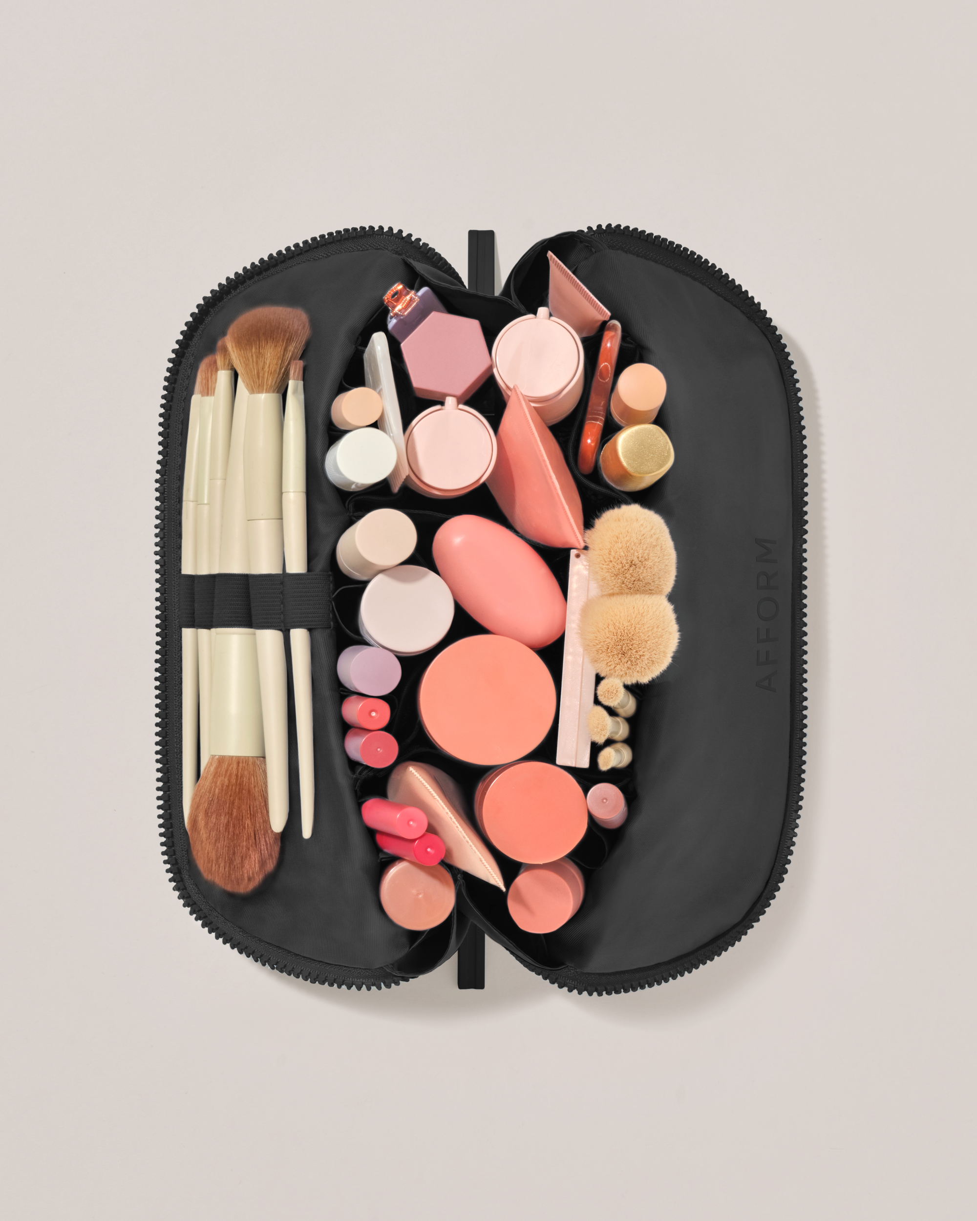 Overhead view of the Medium Onyx (black) Traveller makeup bag fully packed with upright beauty products and organized compartments