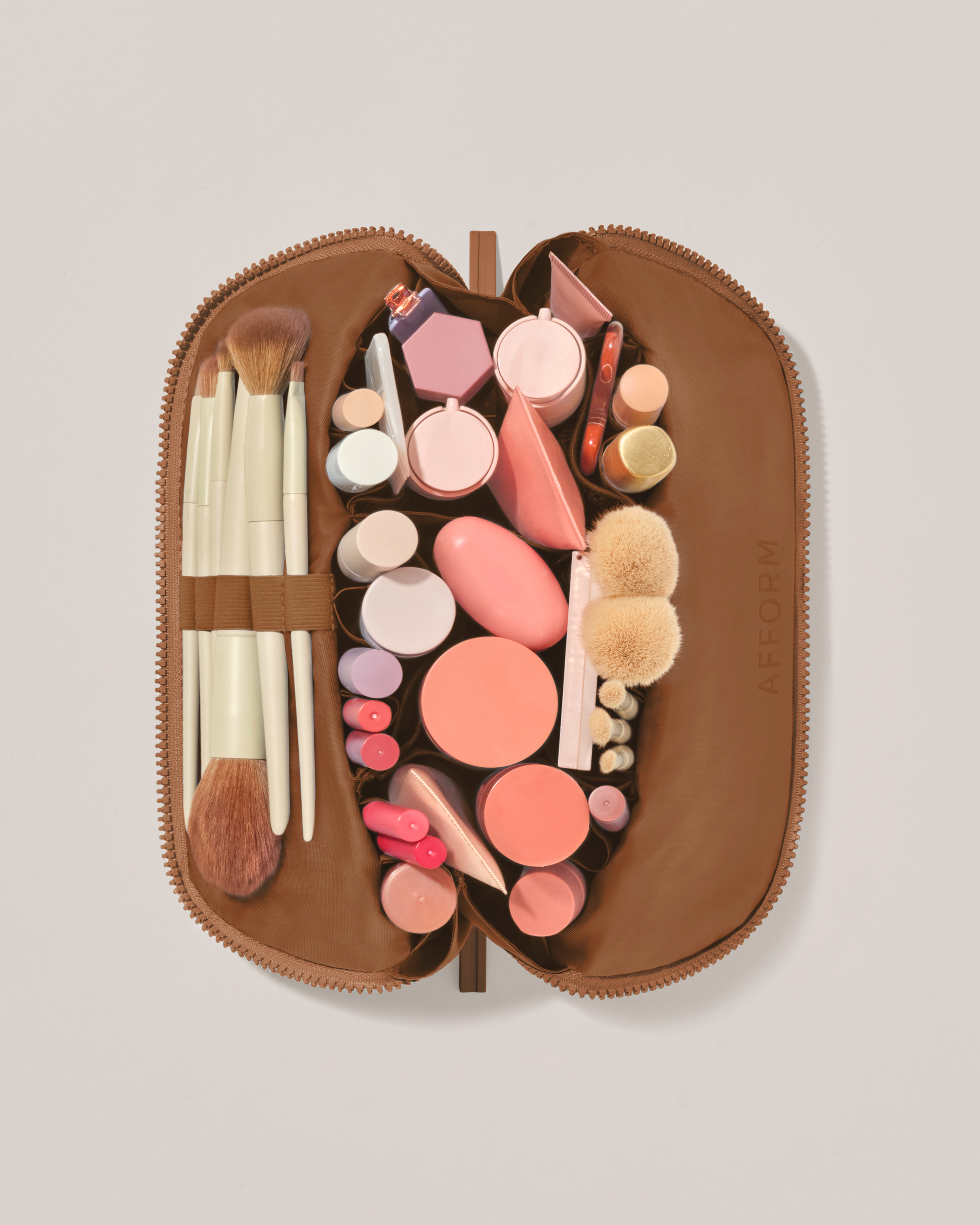 Overhead view of the Medium Vicuna (brown) Traveller makeup bag fully packed with upright beauty products and organized compartments