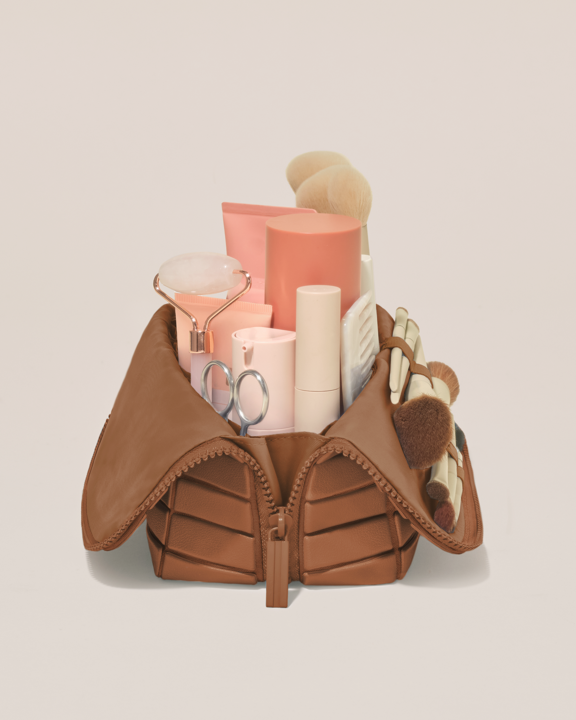 Side profile of the Medium Vicuna (brown) Traveller makeup bag filled with beauty essentials standing upright, showing flexible compartment design