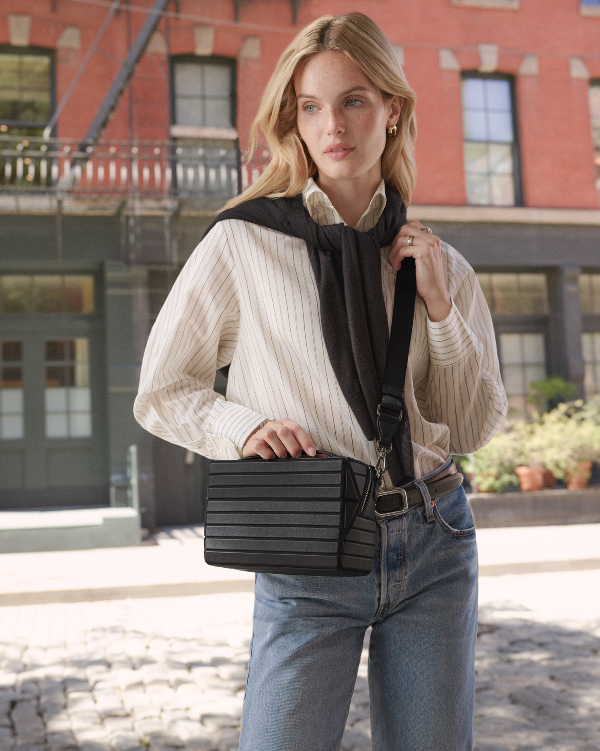 Model wearing the Afform Onyx Crossbody bag with a striped shirt and jeans on a city street
