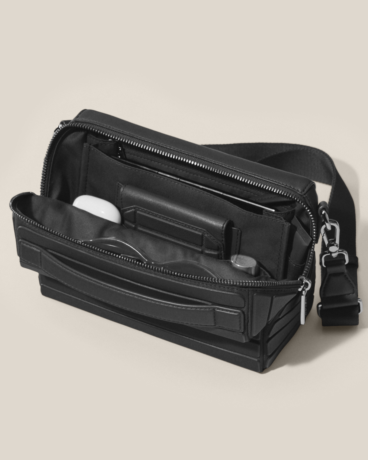 Open Afform Vicuna Crossbody bag showing earbuds, sunglasses, phone, and organized interior pockets