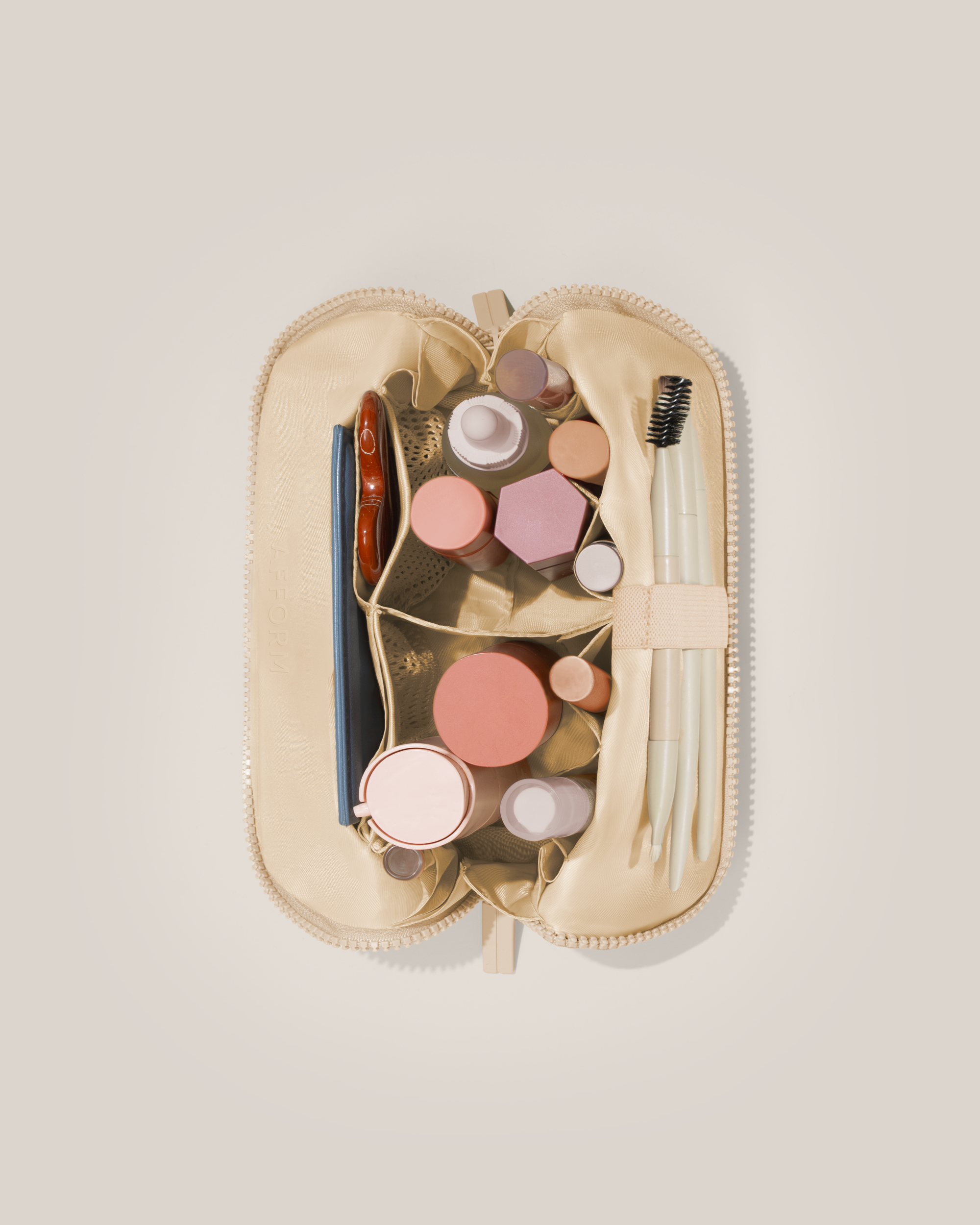 Overhead view of the Small Bisque (white) Traveller makeup bag fully packed with upright beauty products and organized compartments