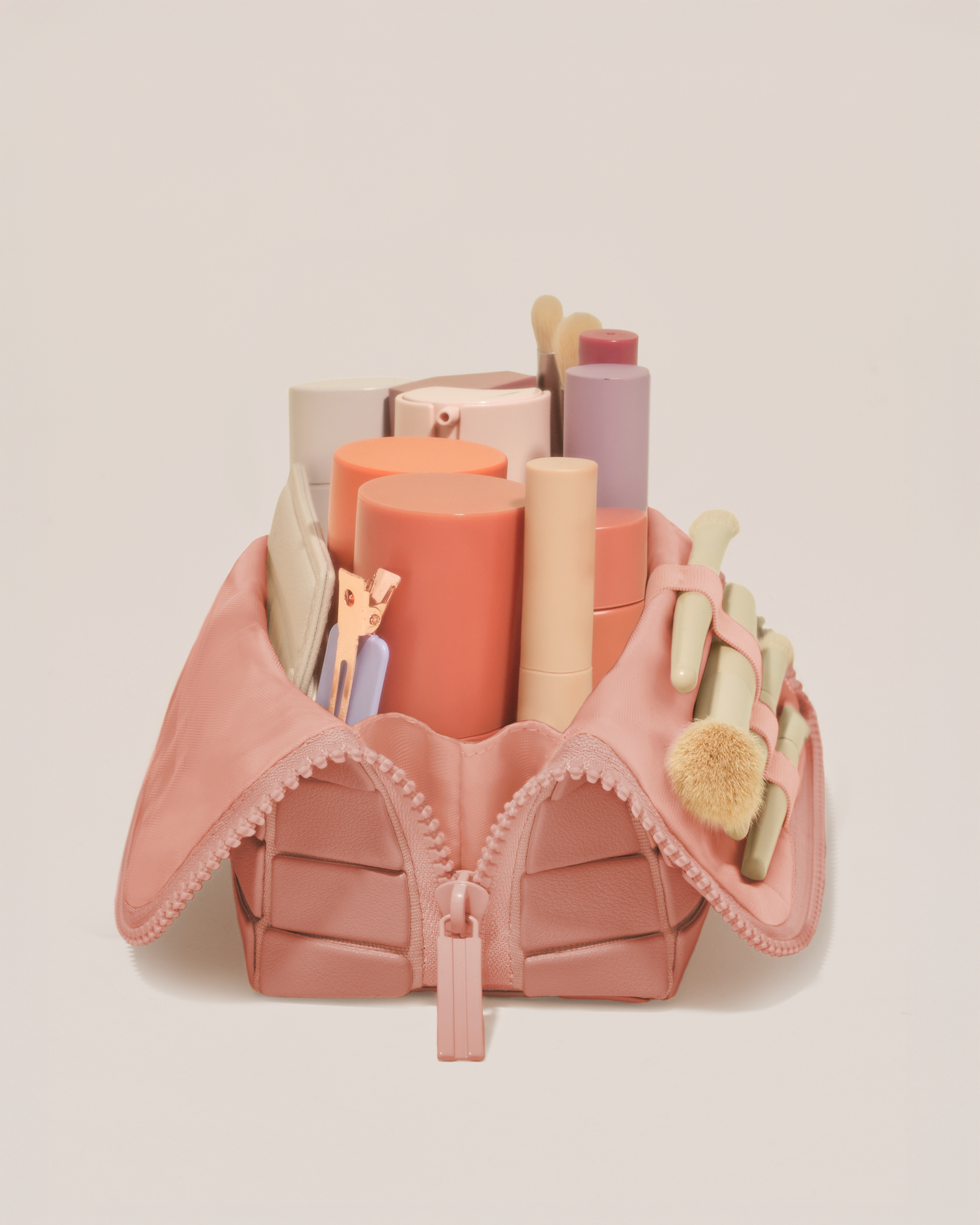 Side profile of the Small Blush (pink) Traveller makeup bag filled with beauty essentials standing upright, showing flexible compartment design
