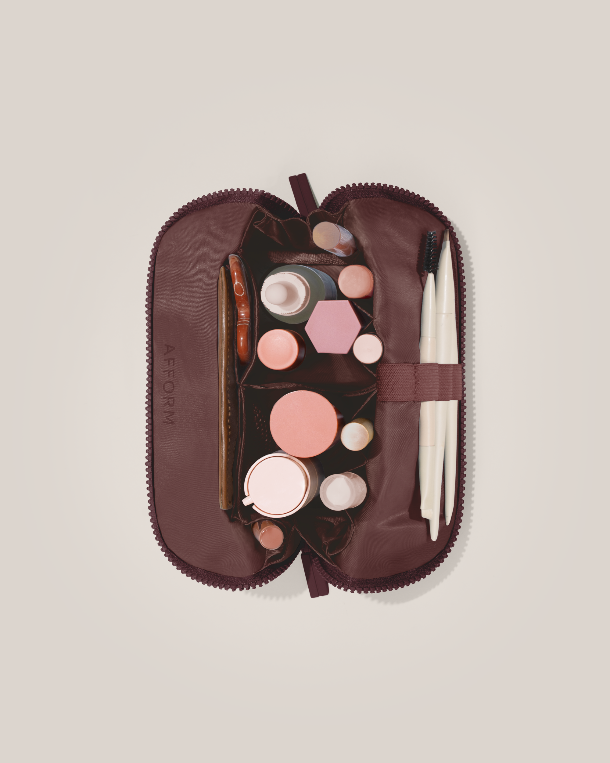 Overhead view of the Small Cassis (maroon) Traveller makeup bag fully packed with upright beauty products and organized compartments