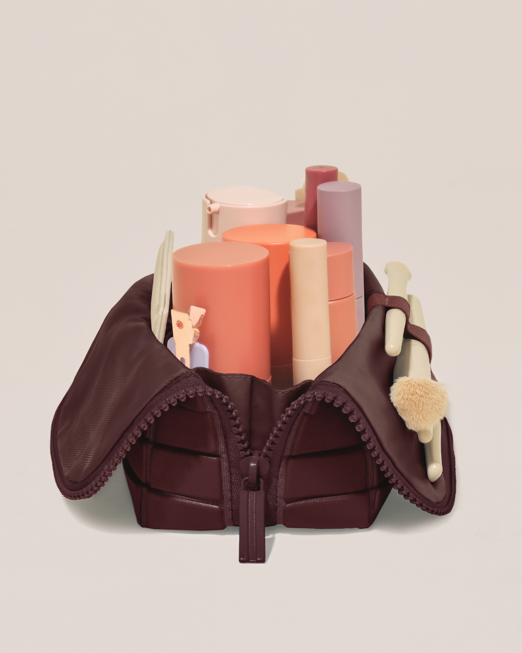 Side profile of the Small Cassis (maroon) Traveller makeup bag filled with beauty essentials standing upright, showing flexible compartment design