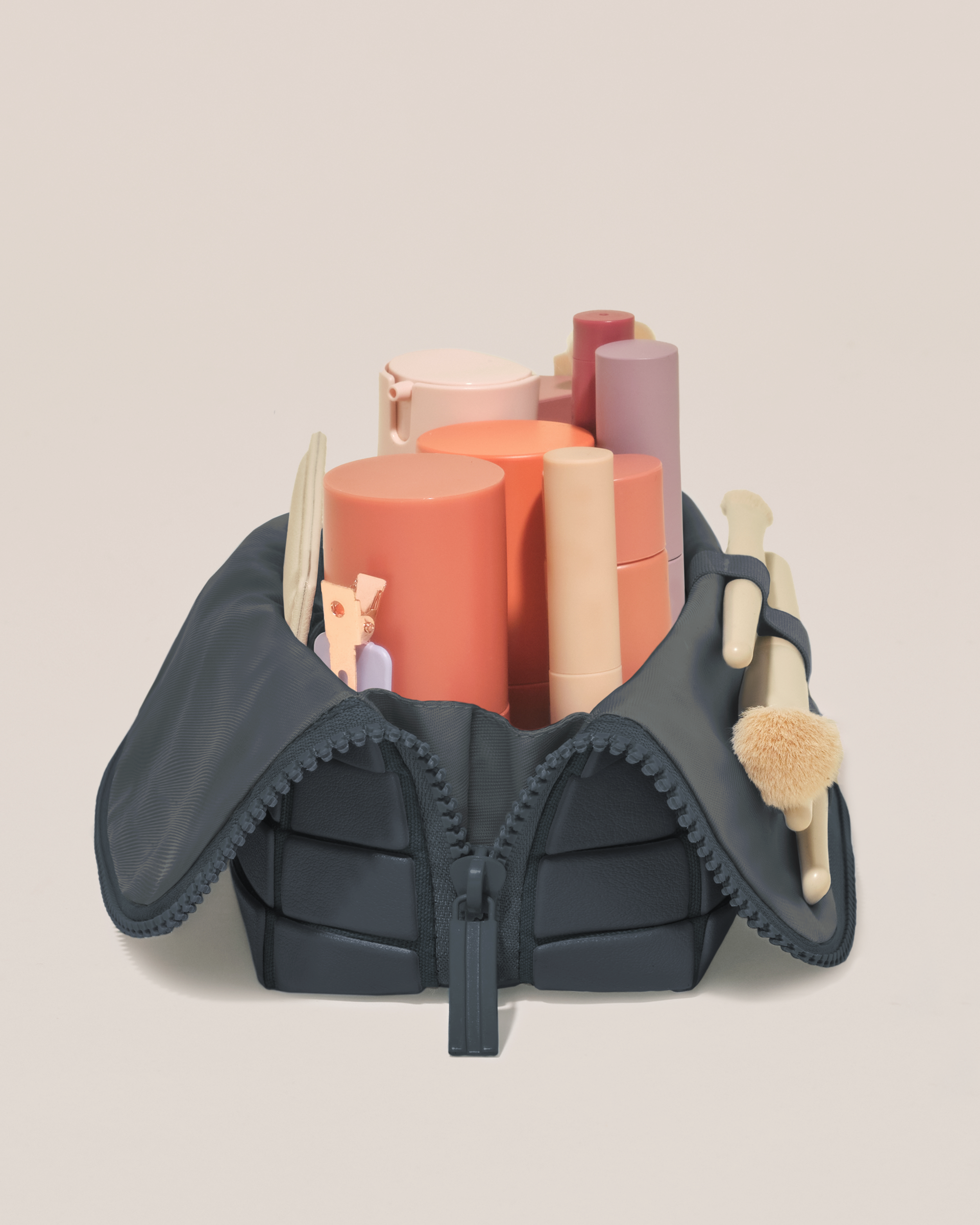 Side profile of the Small Indigo (navy) Traveller makeup bag filled with beauty essentials standing upright, showing flexible compartment design