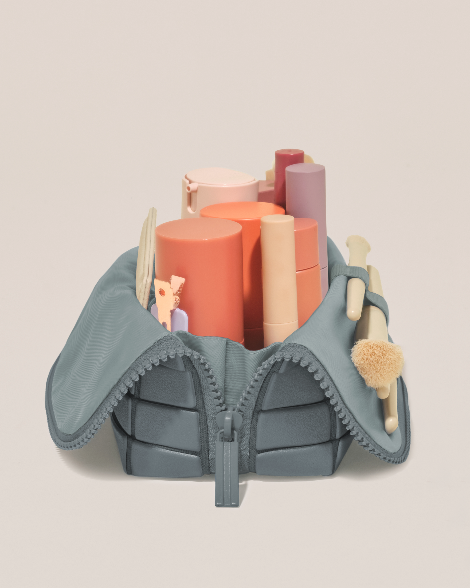 Side profile of the Small Slate (blue) Traveller makeup bag filled with beauty essentials standing upright, showing flexible compartment design