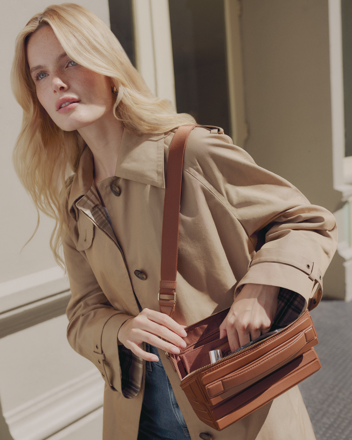 Model in a trench coat reaching into the open Afform Vicuna Crossbody bag worn over the shoulder