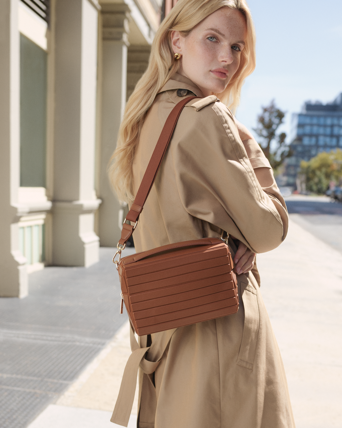 Model wearing the Afform Vicuna Crossbody bag over the shoulder with a trench coat on a city street
