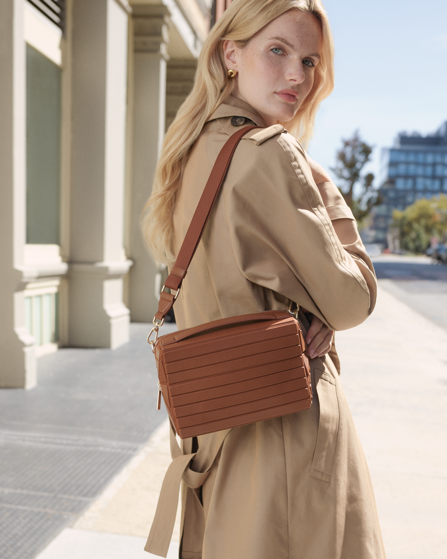 Model wearing the Afform Vicuna Crossbody bag over the shoulder with a trench coat on a city street