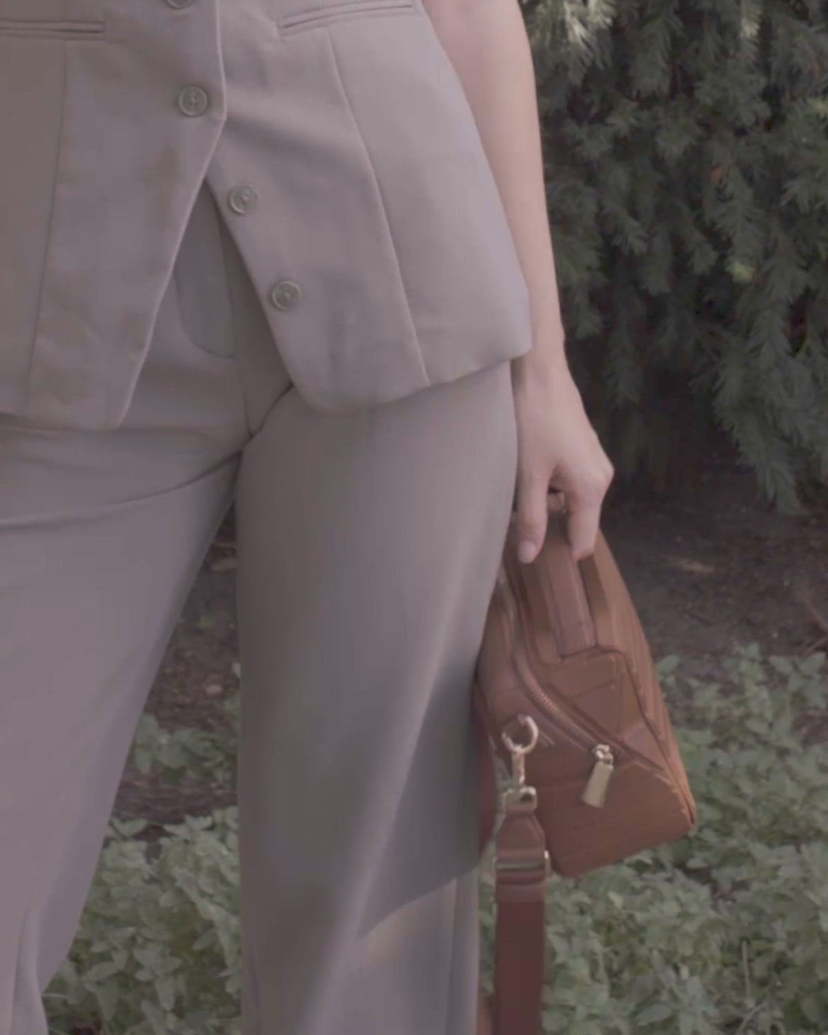 Video of a model wearing the Afform Vicuna Crossbody bag over the shoulder with a neutral vest and trousers outdoors